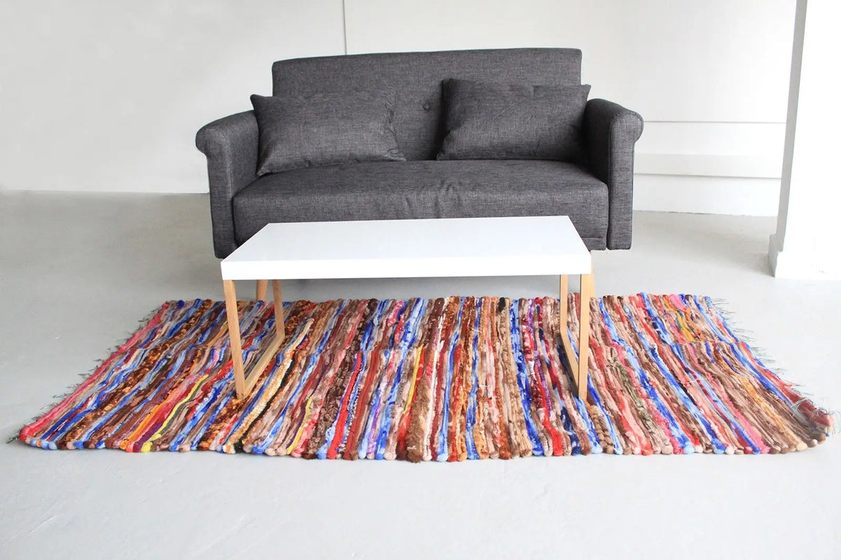Alfombra de trapo rectangular (105x185cm) con rayas multicolores, estilo indio, tejida a mano sobre fondo blanco.
