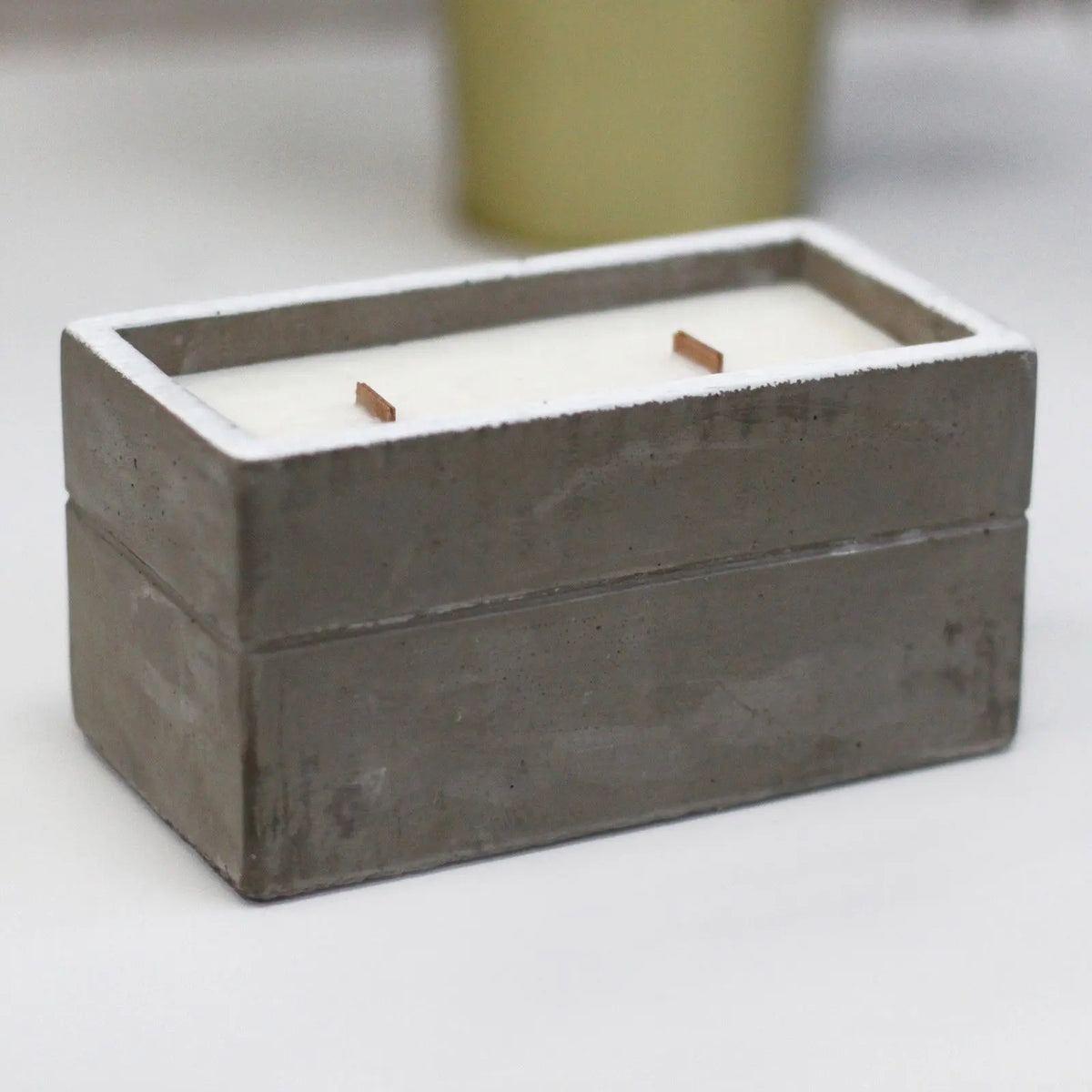 Vela rectangular de cera blanca con dos mechas de madera en un recipiente de hormigón gris de estilo industrial moderno