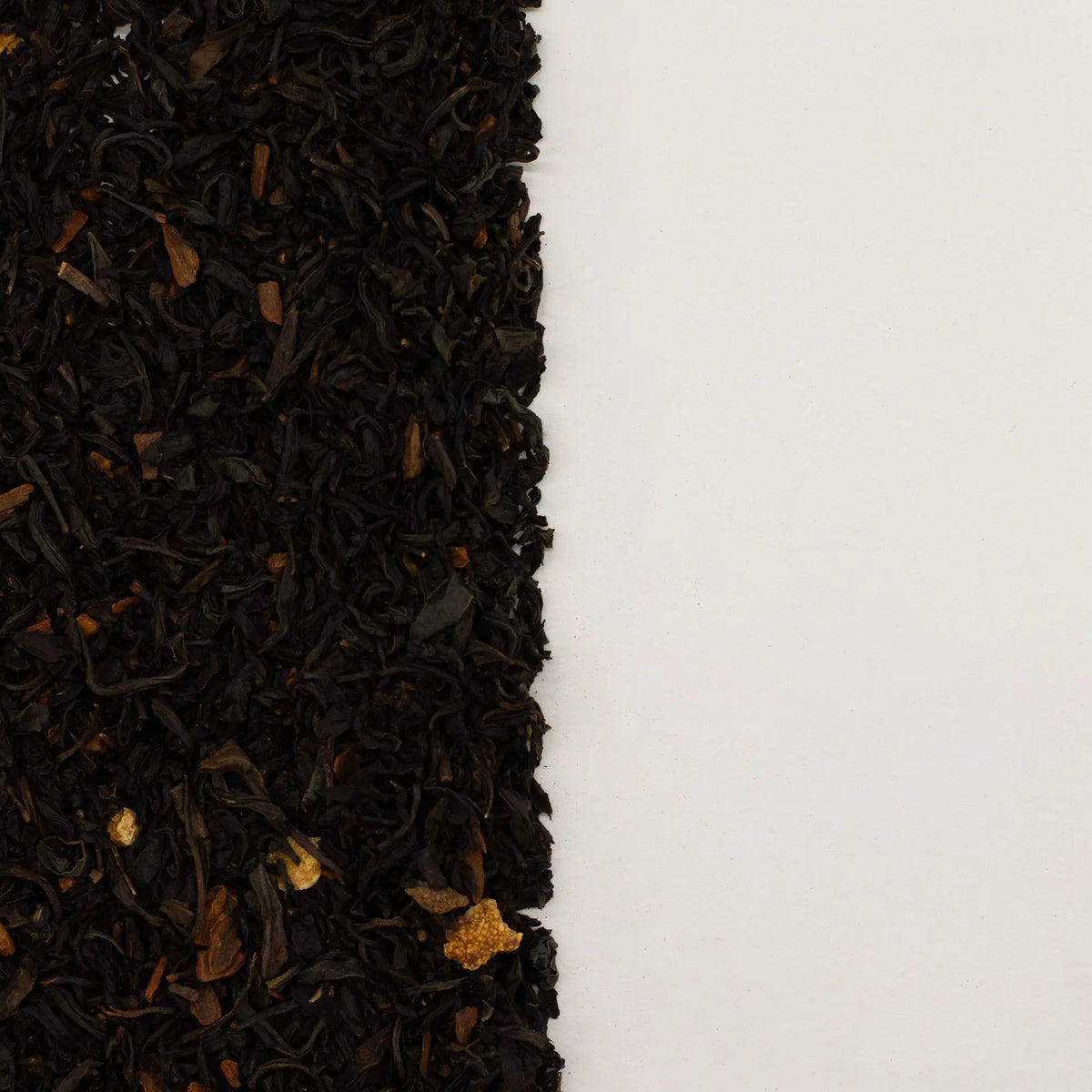 Hojas de té negro seco mezcladas con trozos de cáscara de naranja sobre fondo blanco liso.