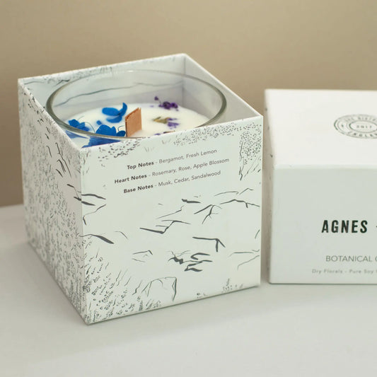 Vela de soya blanca con notas de bergamota y rosa, en caja decorativa con dibujos botánicos en negro.