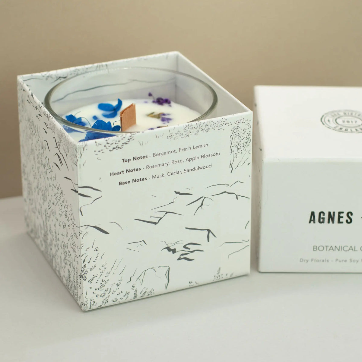 Vela de soya blanca con notas de bergamota y rosa, en caja decorativa con dibujos botánicos en negro.