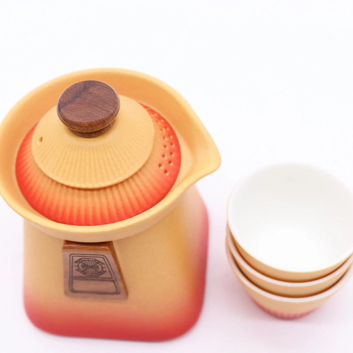 Juego de tetera de cerámica naranja con degradado rojo, tapa con pomo de madera y tres tazas a juego.