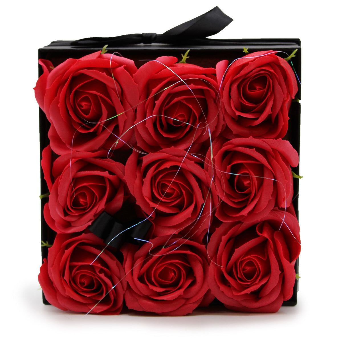 Caja cuadrada negra con 9 rosas rojas de jabón dispuestas en cuadrícula, decorada con un lazo y finos hilos brillantes.