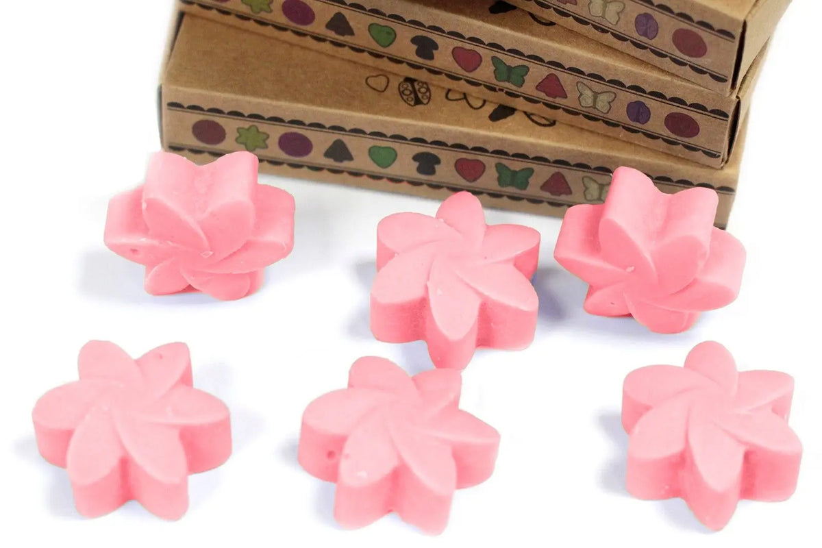 Seis ceras de soja rosas con forma de flor frente a cajas de cartón artesanal con diseños decorativos de estilo rústico