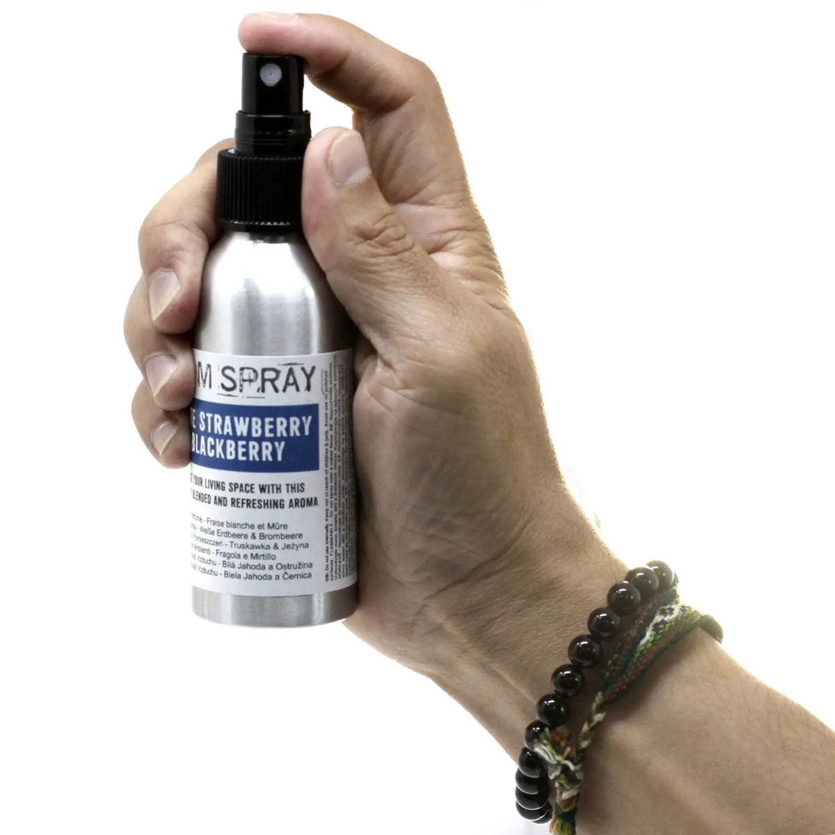 Mano sosteniendo un frasco metálico de ambientador en spray de 100 ml con etiqueta informativa sobre fondo blanco.