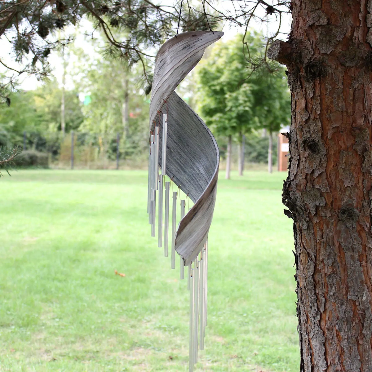 Campanilla de viento de hoja de coco blanqueada en forma de espiral con tubos metálicos colgando de un árbol.