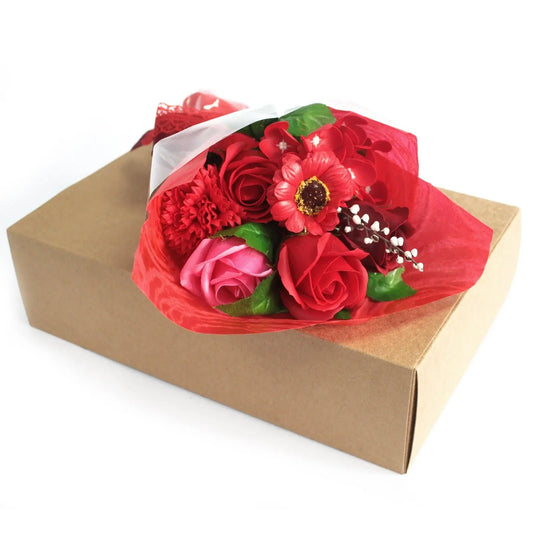 Ramo de flores de jabón rojas y rosadas envuelto en papel decorativo, sobre una caja de cartón rectangular color kraft.