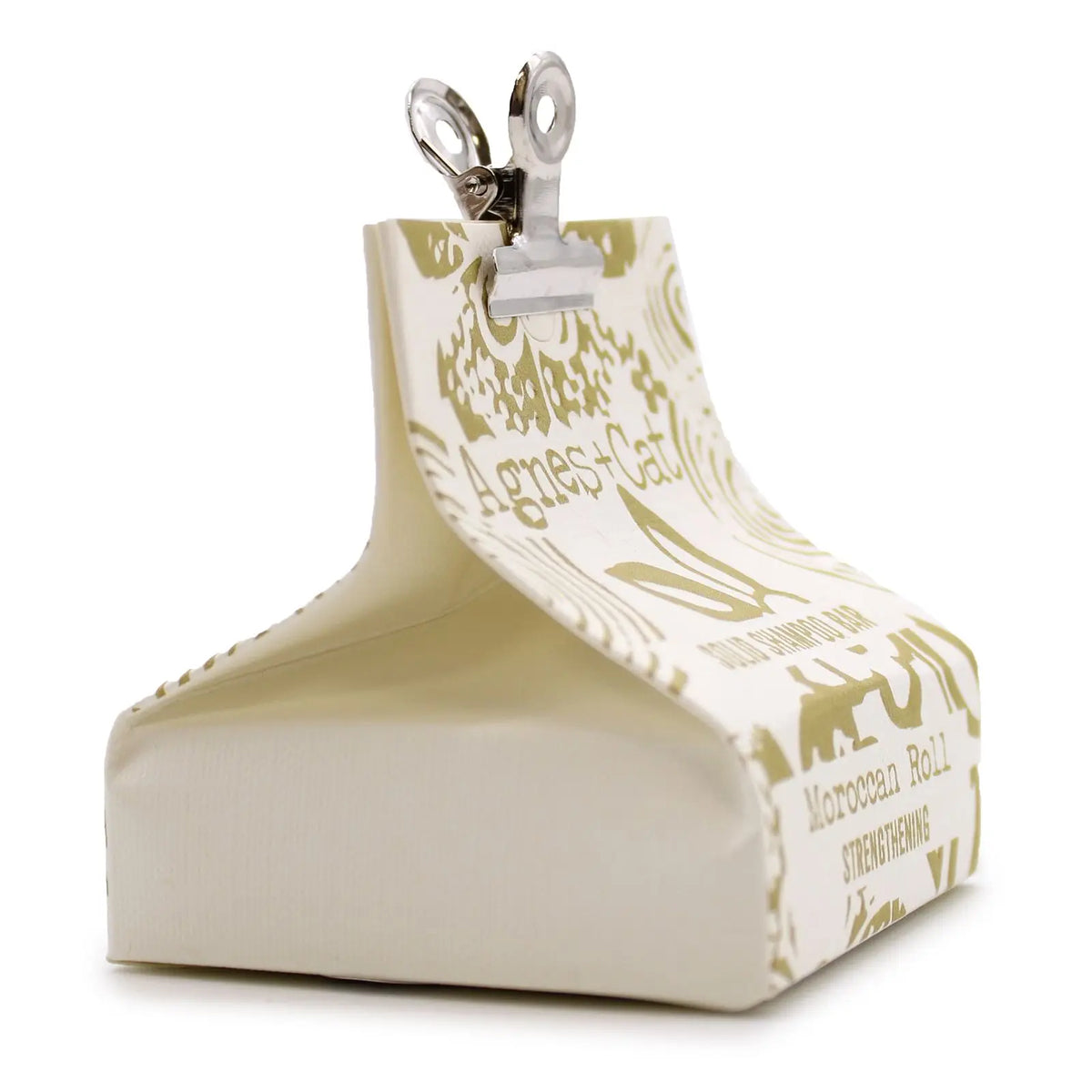 Champú sólido Agnes+Cat envuelto en papel crema con estampado dorado, cerrado con una pinza metálica sobre fondo blanco.