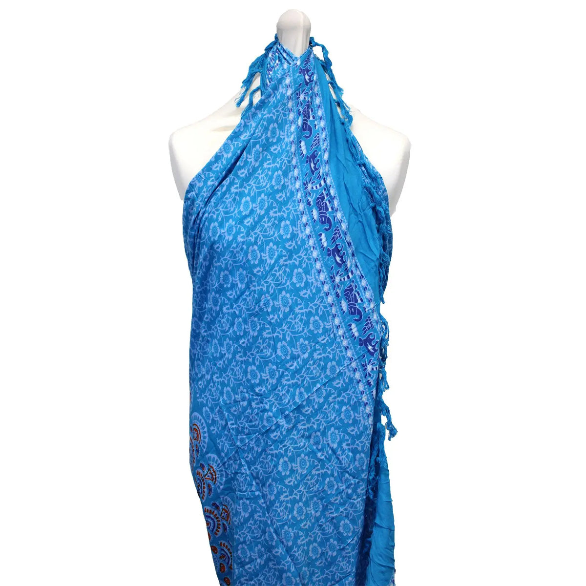 Pareo azul con estampado floral y cenefa de elefantes, atado al cuello sobre un maniquí. Flecos en los laterales.