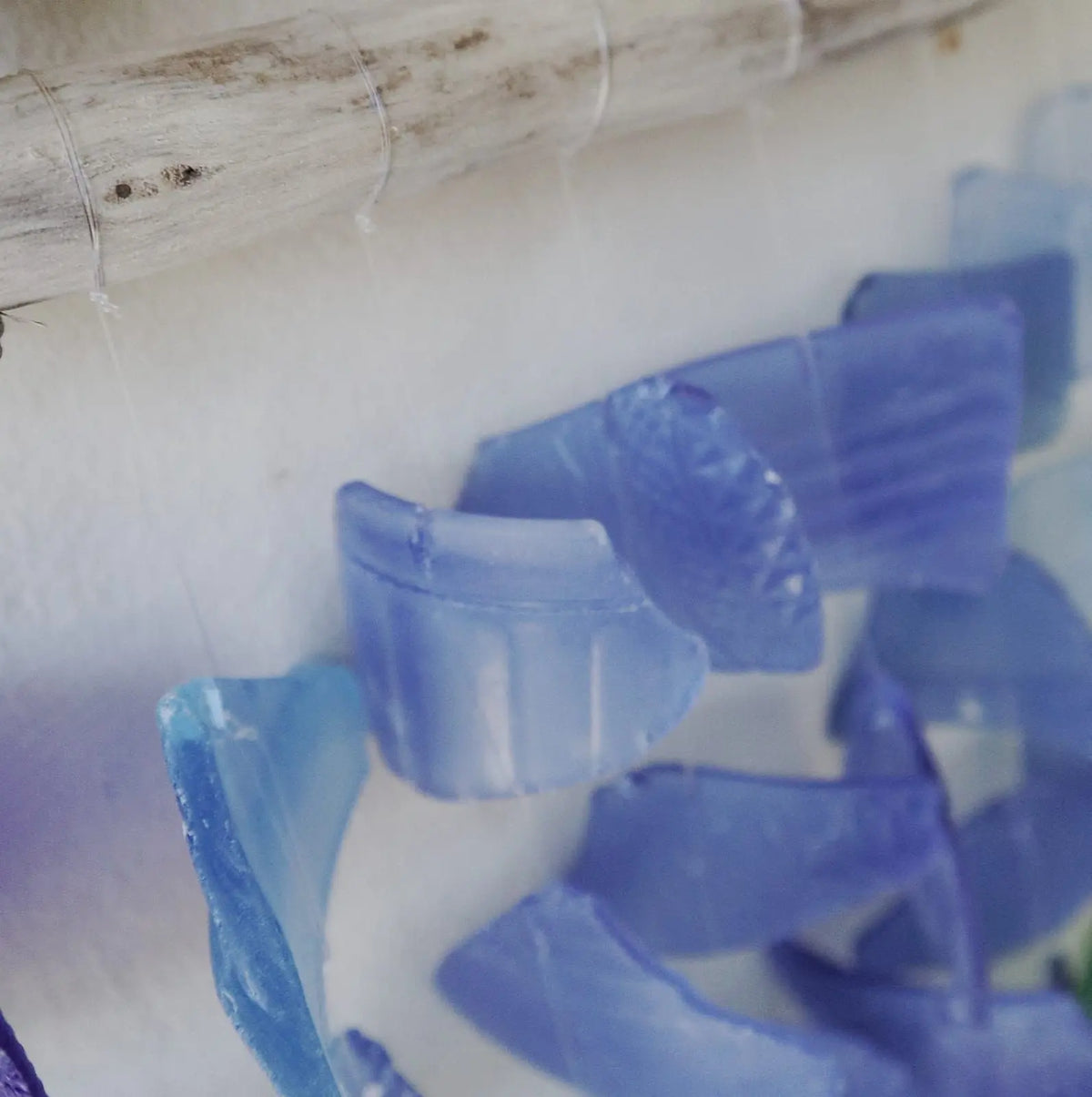 Carrillón con piezas de vidrio reciclado azul traslúcido suspendidas de una rama de madera natural.