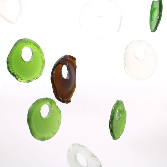 Carillón artesanal con fondos de botella de vidrio reciclado verde, marrón y transparente colgando sobre fondo blanco.