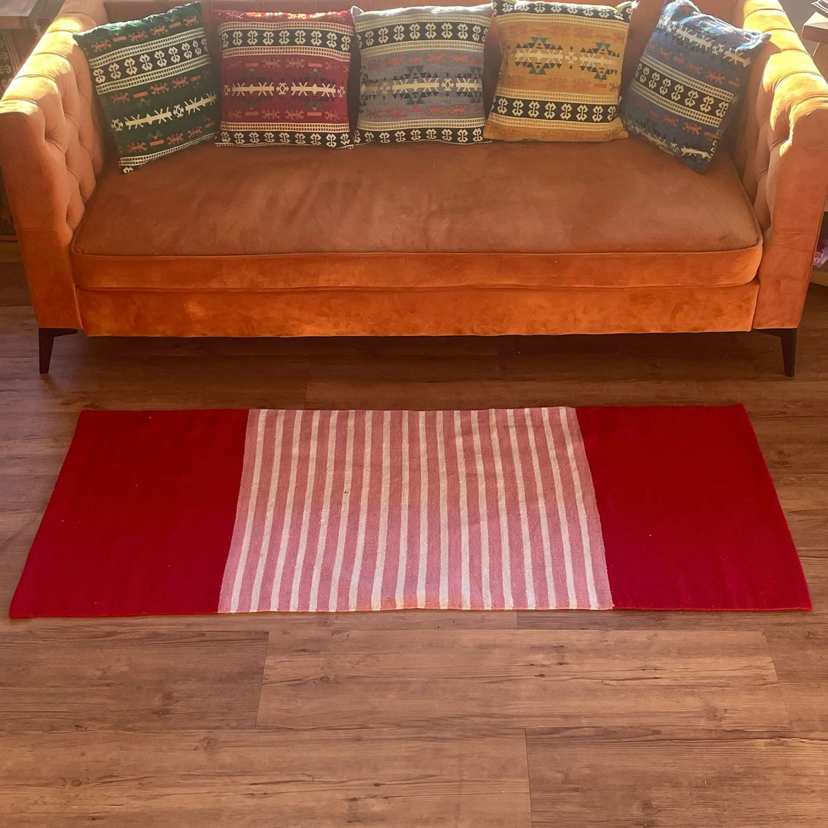 Alfombra rectangular de algodón con bandas rojas laterales y franjas verticales rosa y blancas en el centro.