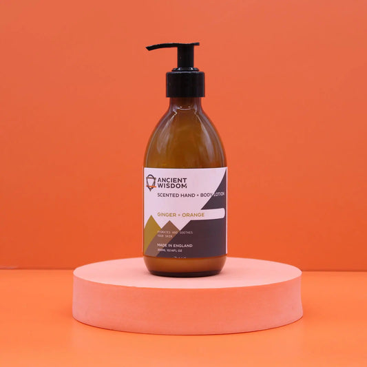 Botella de vidrio ámbar con dispensador negro sobre base rosa, fondo naranja, etiqueta de jengibre y naranja de 300ml.