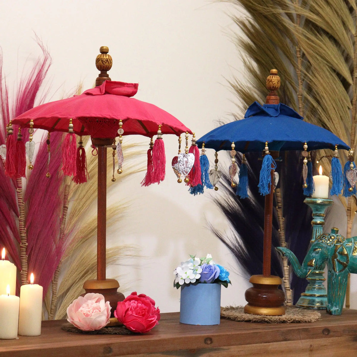 Dos sombrillas decorativas de algodón, una roja y otra azul, con borlas, cuentas y base de madera sobre una mesa.