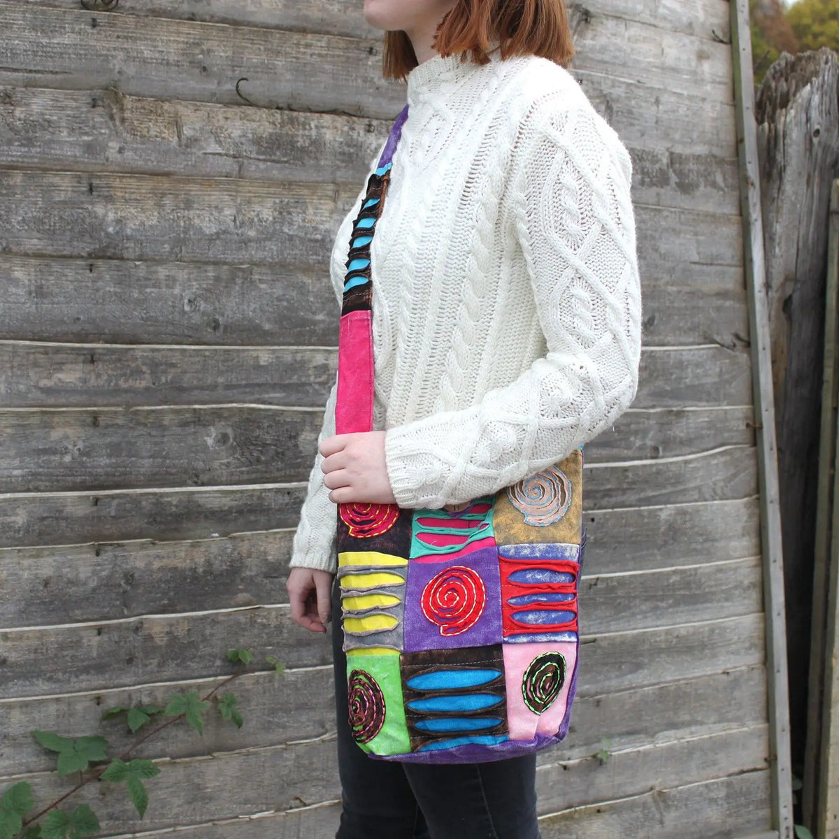 Bolso bandolera de estilo bohemio con parches coloridos, patrones de espirales bordadas y tela texturizada.