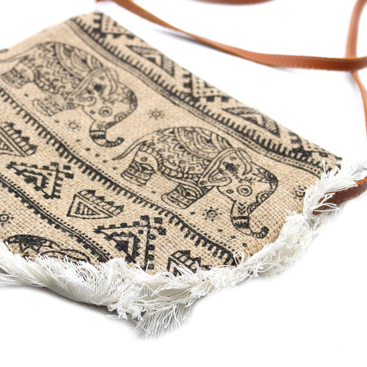 Bolso bandolera de yute color beige con estampado de elefantes en negro, flecos blancos inferiores y correa marrón.