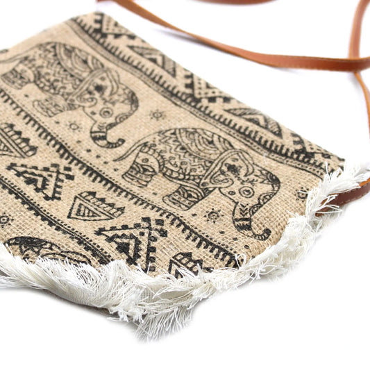 Bolso bandolera de yute color beige con estampado de elefantes en negro, flecos blancos inferiores y correa marrón.