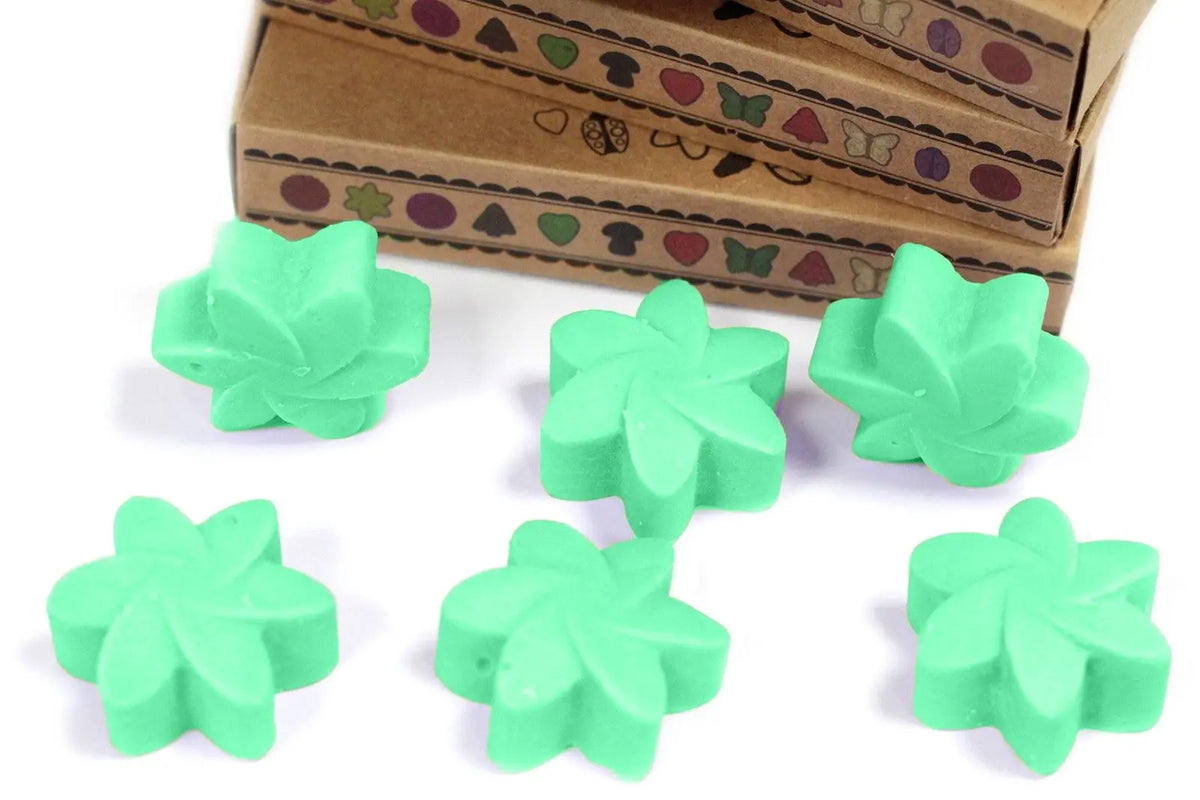 Seis ceras de soja verde en forma de flor frente a cajas de cartón con motivos de jardín sobre fondo blanco.