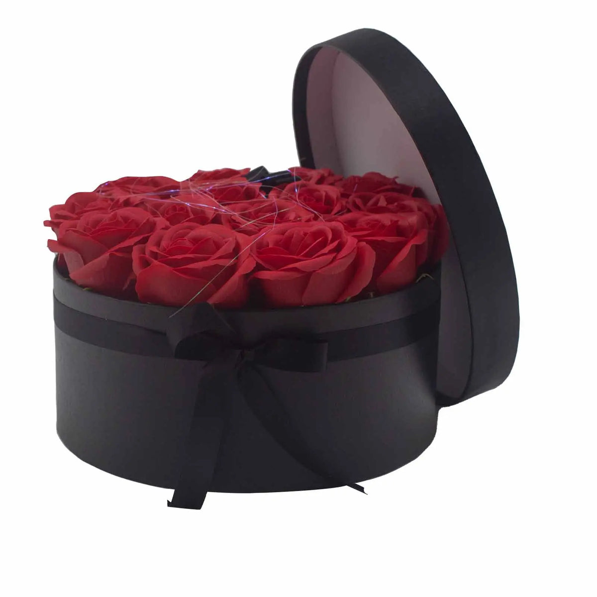Caja redonda negra con 14 rosas rojas de jabón, decorada con un lazo negro. Tapa abierta inclinada. Fondo blanco.