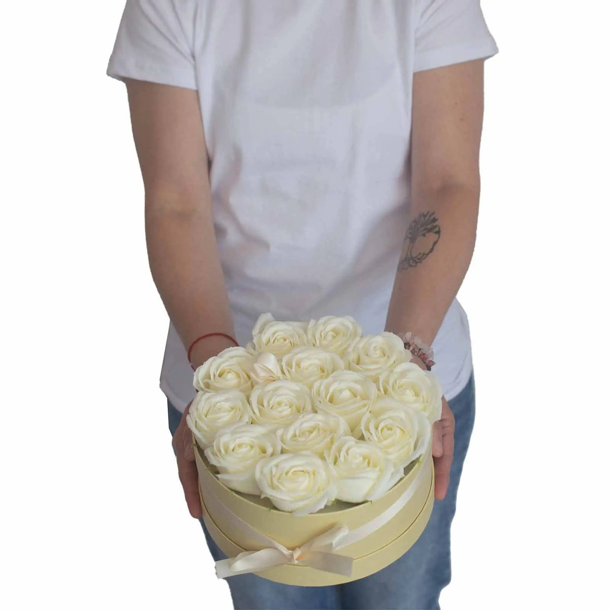 Caja redonda crema con 13 rosas de jabón blancas, sostenida por una persona en camiseta blanca.