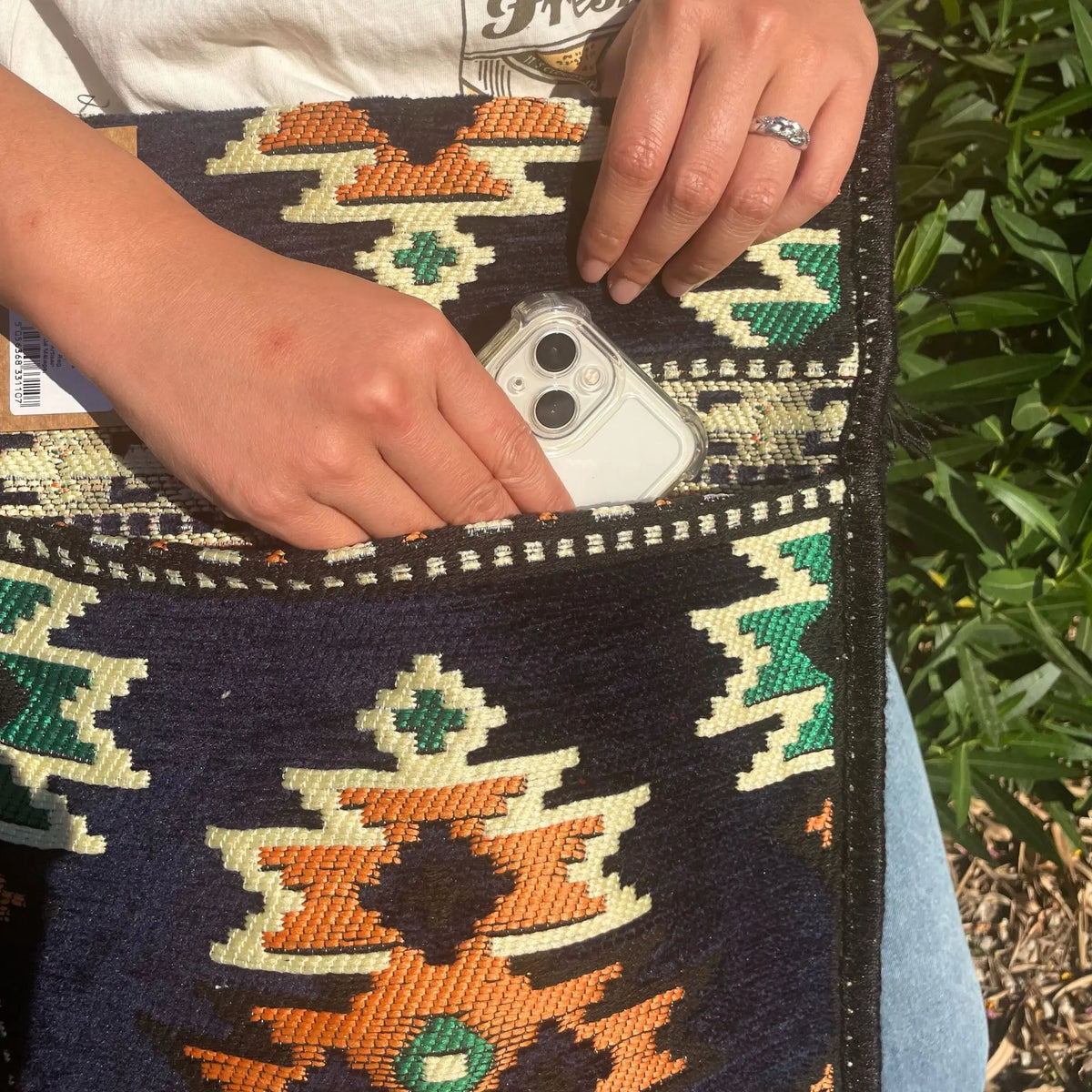 Bolso bandolera de tela con patrón Kilim azul marino, verde y naranja, con un teléfono guardado en su bolsillo frontal.