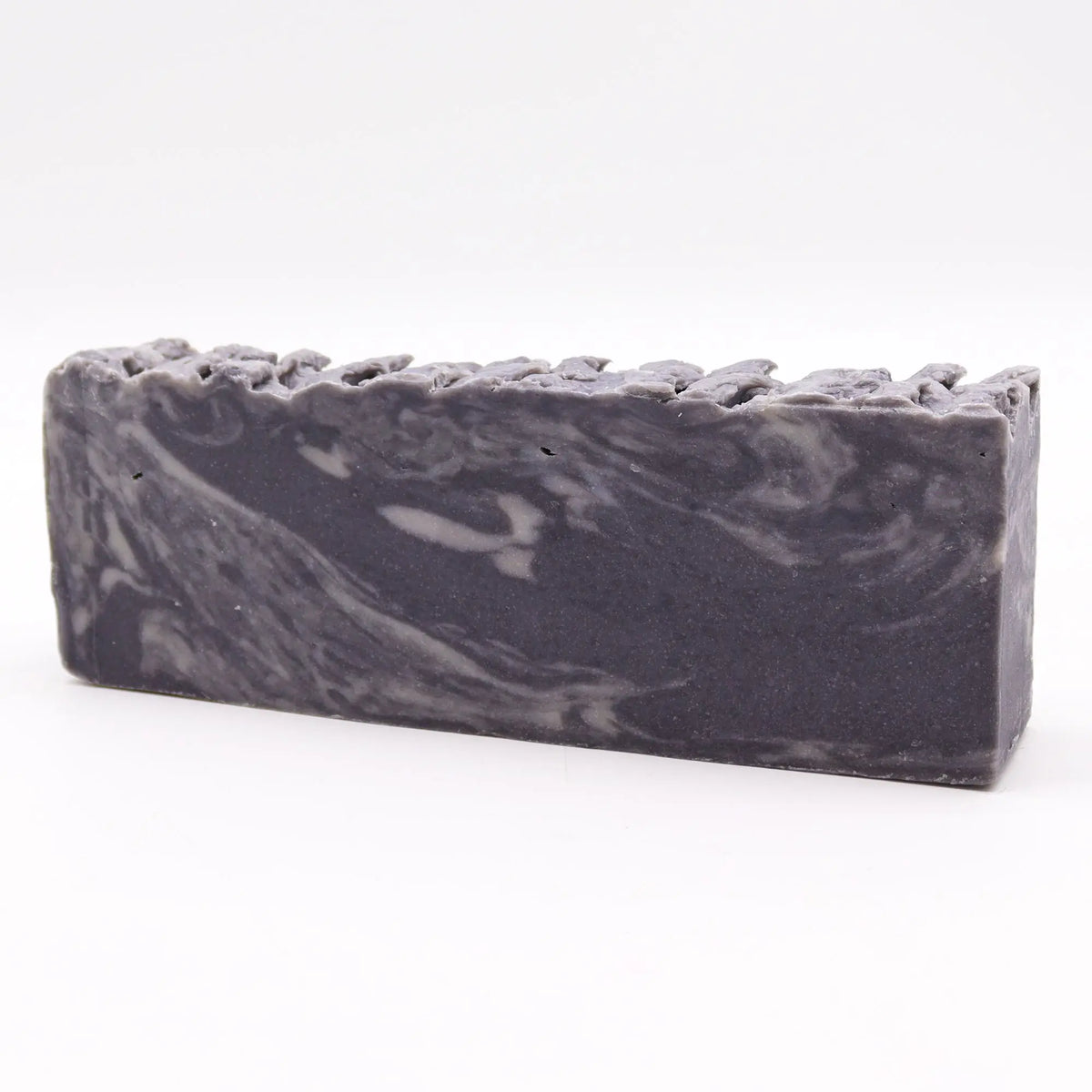 Barra de jabón artesanal rectangular, color gris jaspeado con veteado blanco y borde superior irregular y texturizado.