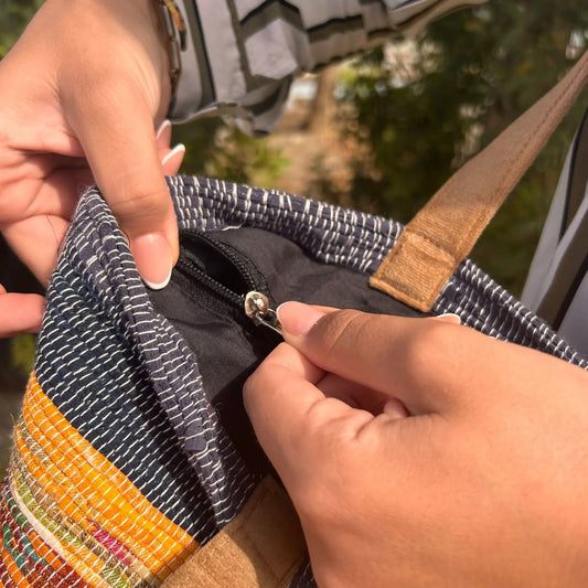 Bolso grande tejido de materiales reciclados con texturas, tonos tierra y detalle de cierre con forro negro interior.