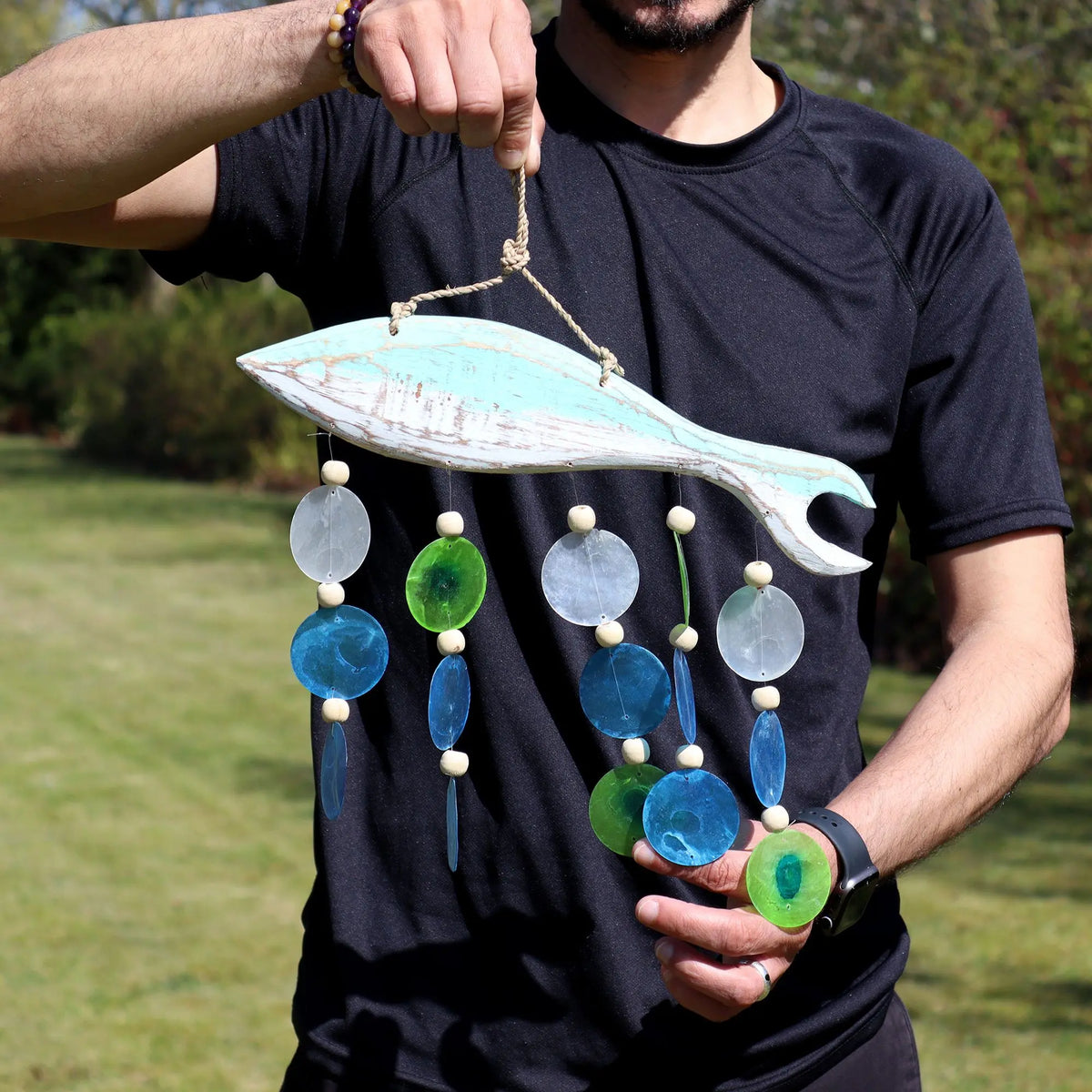 Carillón de madera con forma de pez rústico color aqua, decorado con colgantes de discos translúcidos azules y verdes.