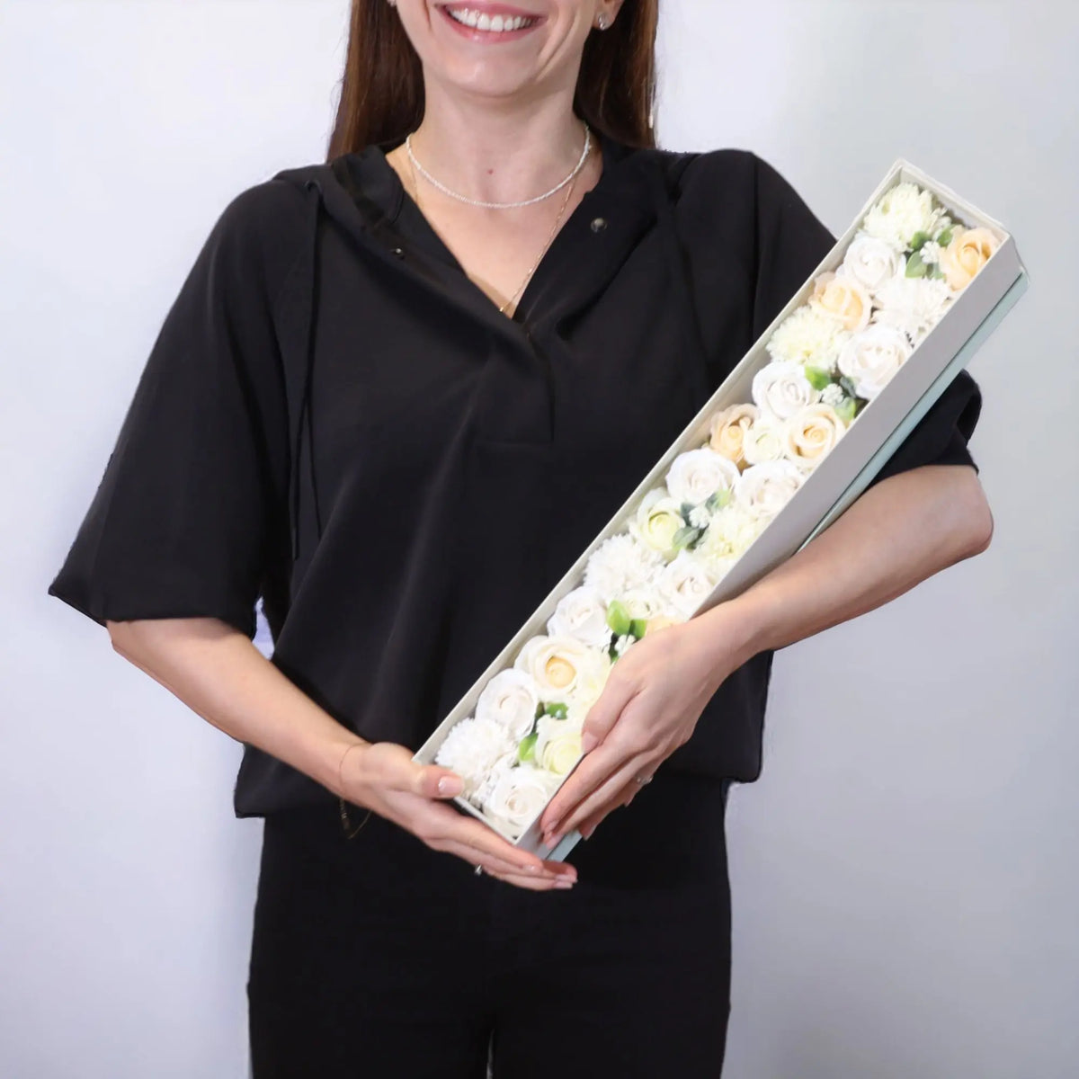 Persona sosteniendo caja alargada con flores de jabón en tonos blanco y marfil, estilo elegante para regalo.