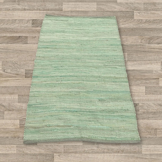 Alfombra rectangular pequeña de algodón tejido a mano, color verde con textura lineal, sobre suelo de madera.