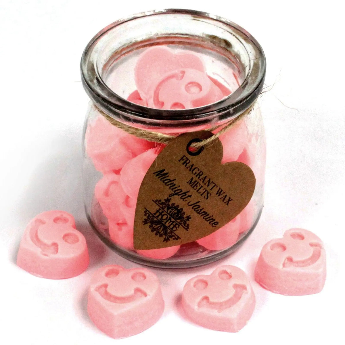 Frasco de vidrio lleno de pastillas de cera de soja rosas en forma de corazón con carita feliz sobre fondo blanco.