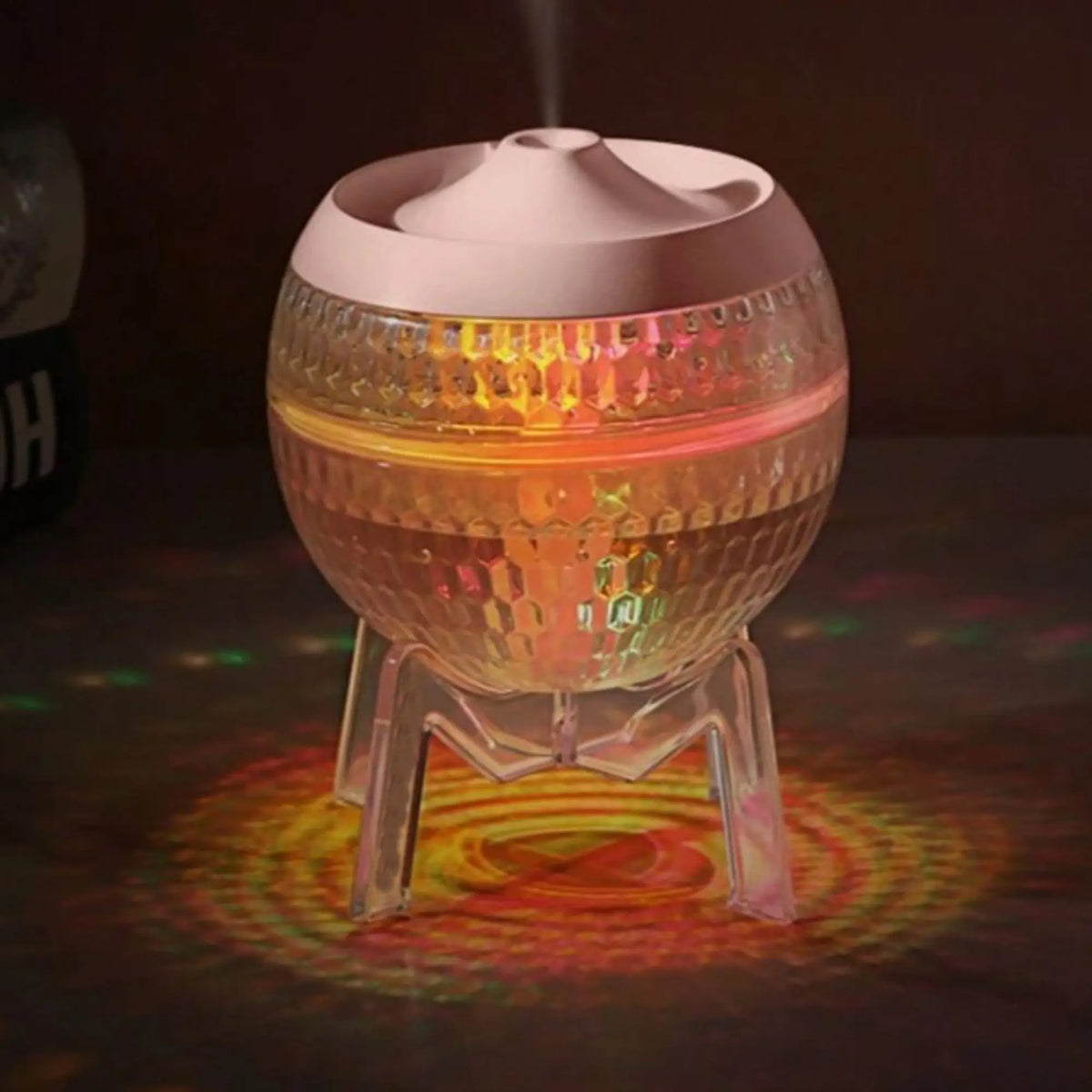 Difusor Mondo Planet esférico, transparente y texturizado, con luces LED que cambian de color y base tipo trípode.