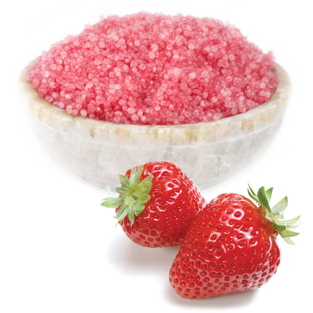 Cuenco de piedra clara lleno de gránulos aromáticos de color rosa intenso junto a dos fresas frescas sobre fondo blanco.