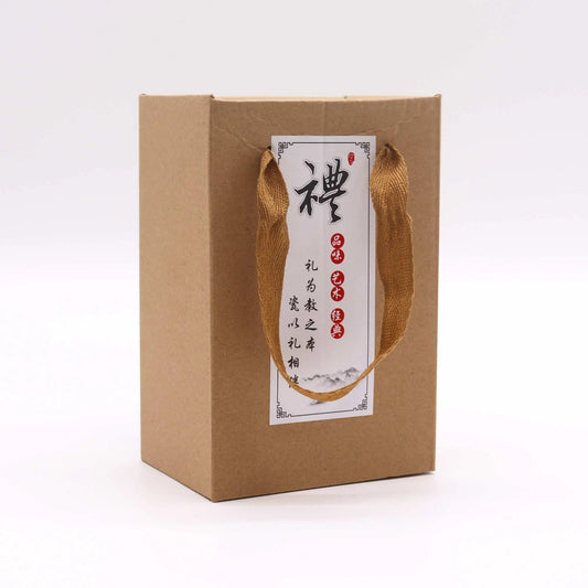 Bolsa de regalo de cartón kraft marrón con asas de tela, etiqueta blanca con caligrafía china y diseño minimalista.