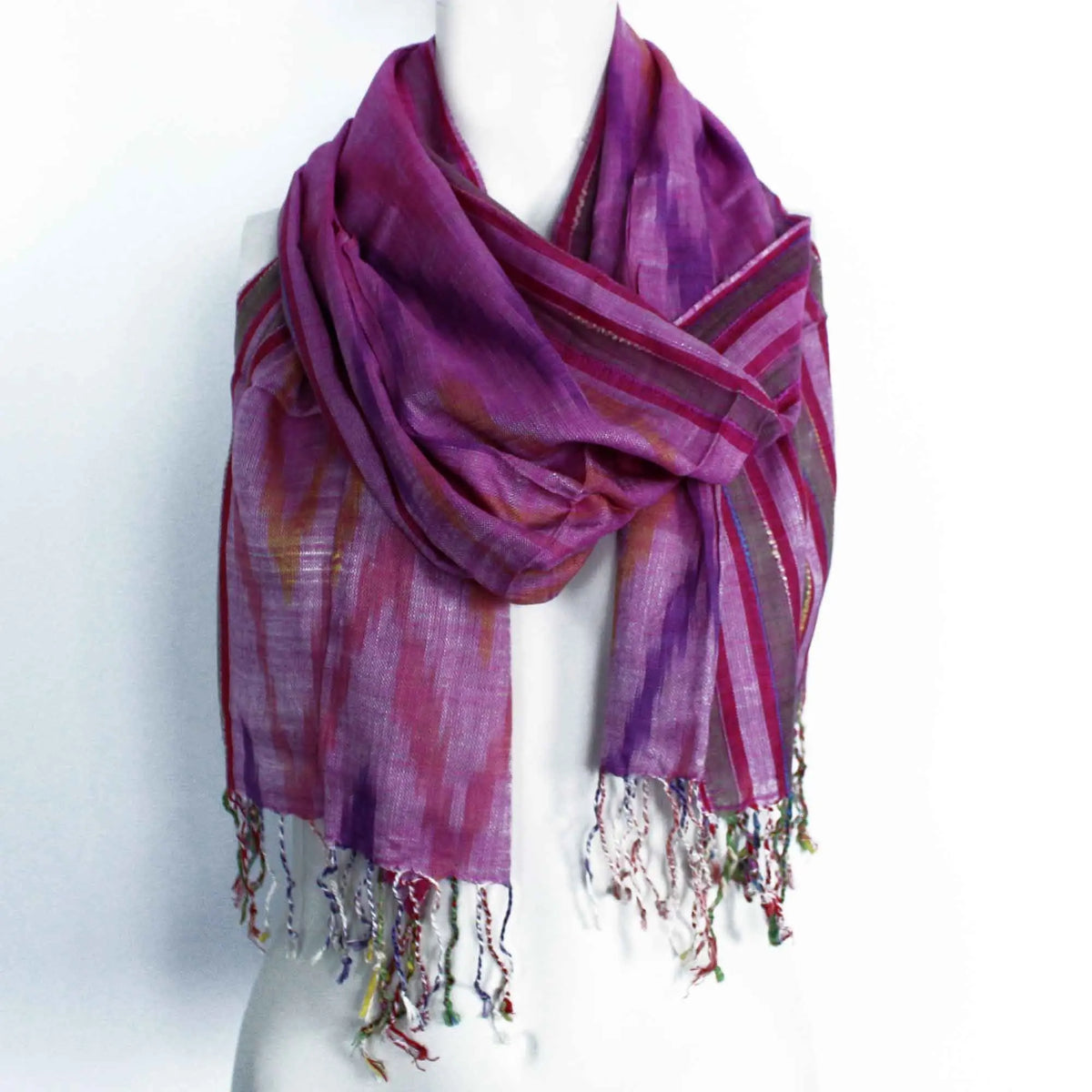 Bufanda bohemia de tela ligera en tonos violeta y magenta con rayas, estampado difuso y flecos multicolores en bordes.