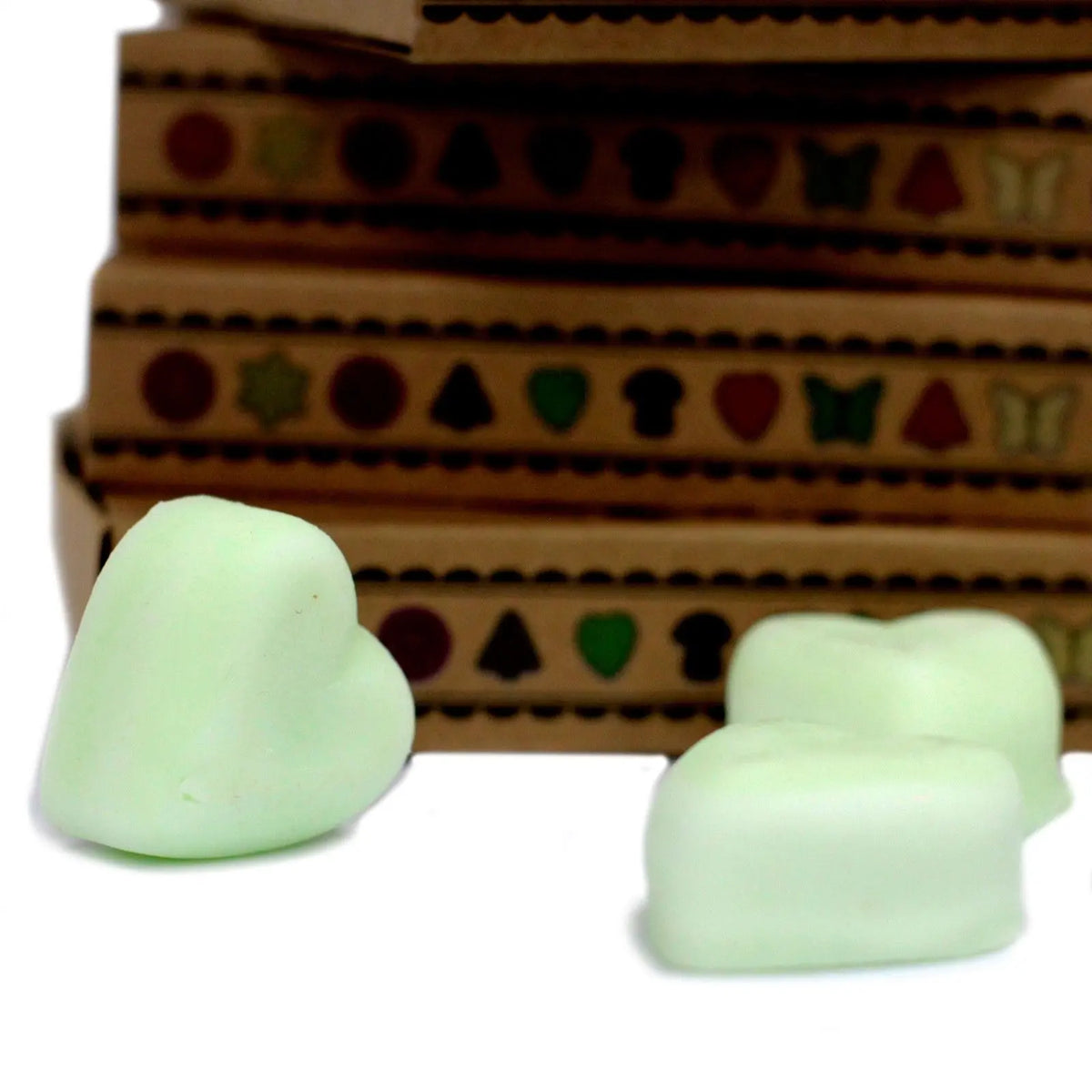 Ceras de soja en forma de corazón color verde claro frente a cajas de regalo de cartón marrón apiladas.