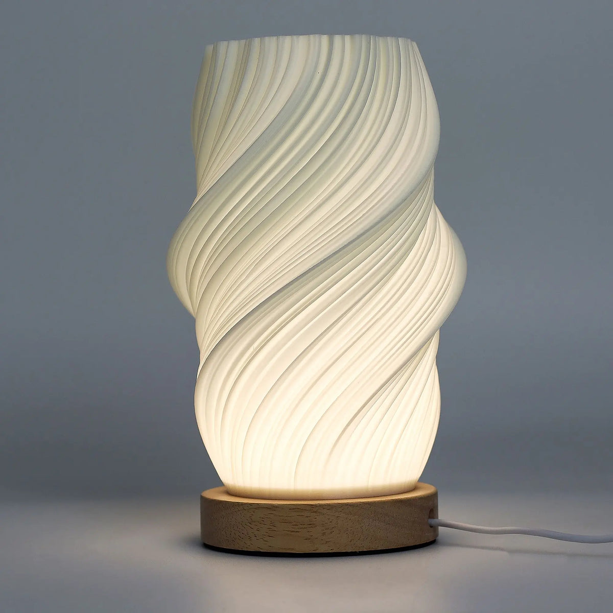 Lámpara de sobremesa con pantalla blanca de textura ondulada y base de madera clara, emitiendo luz ambiental cálida.