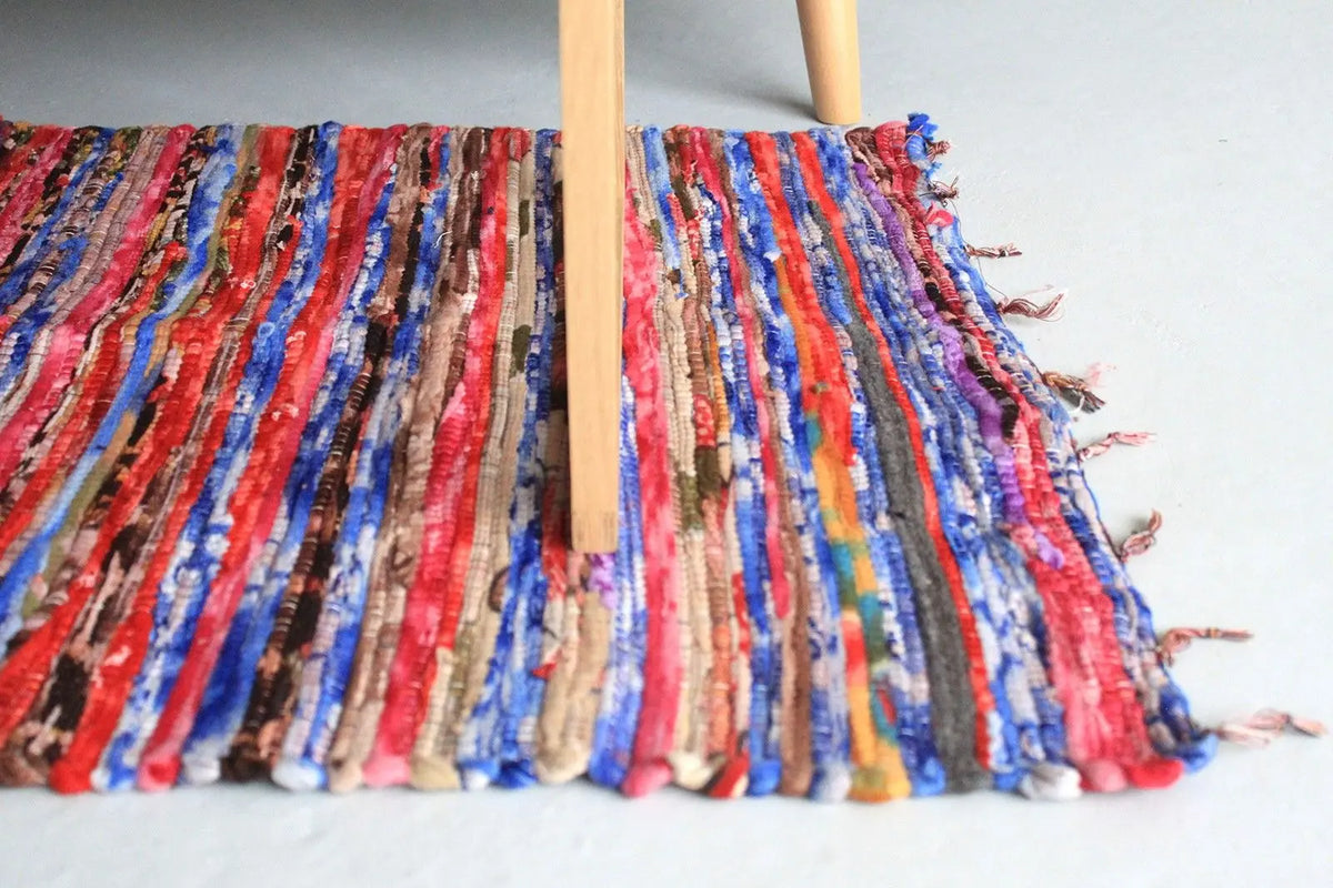 Alfombra india de trapo multicolor, 128x75cm, tejida con tiras de tela en tonos vivos y borde con flecos cortos.