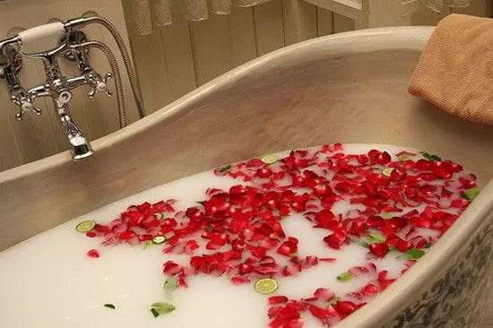 Pétalos de flores de jabón rojas flotando en una bañera con agua blanca estilo spa y detalles de rodajas de lima