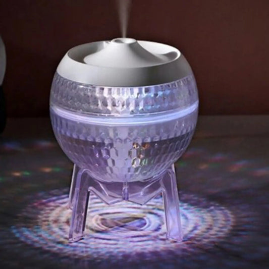 Difusor esférico transparente tipo planeta sobre soporte, emitiendo vapor y luz LED multicolor, marca Ancient Wisdom.