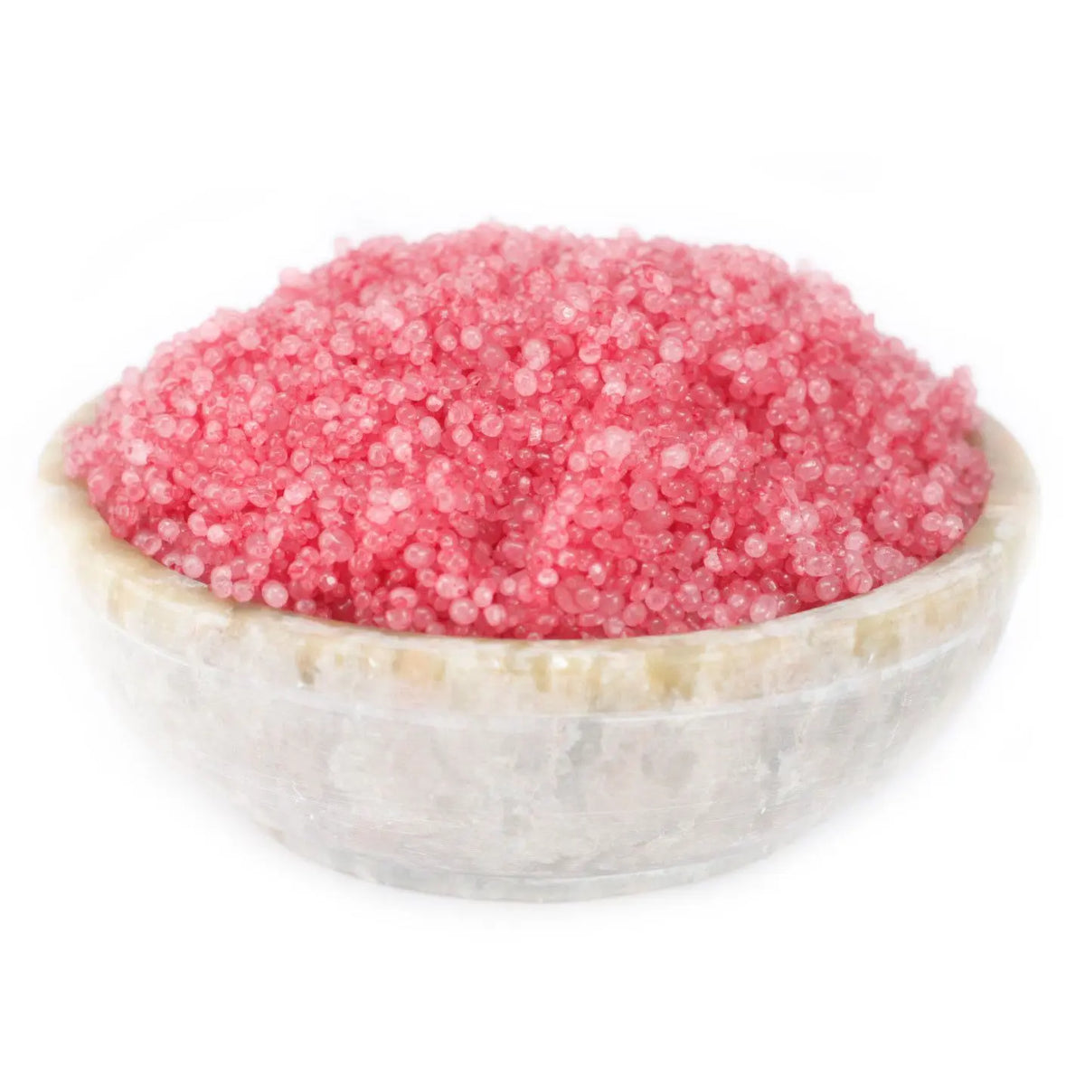 Cuenco de piedra natural lleno de pequeños gránulos aromáticos de color rosa intenso sobre fondo blanco.