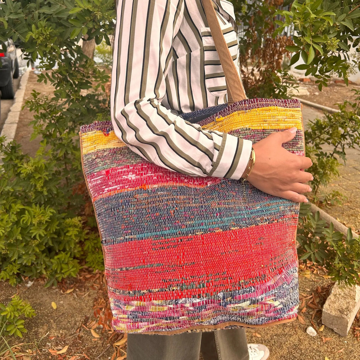Bolso grande tipo tote, tejido artesanal con tiras recicladas de colores vibrantes como rojo, amarillo y azul.