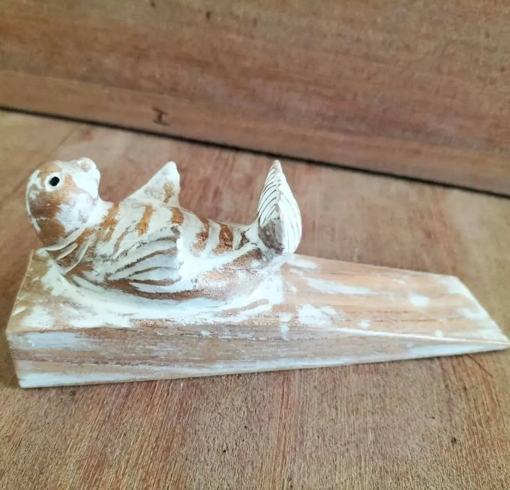 Tope de puerta de madera tallada con forma de cría de foca, acabado rústico en tonos blanco y madera natural.