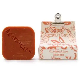 Champú sólido naranja Agnes + Cat, aroma clementina, forma cuadrada y envoltorio de papel con pinza metálica.