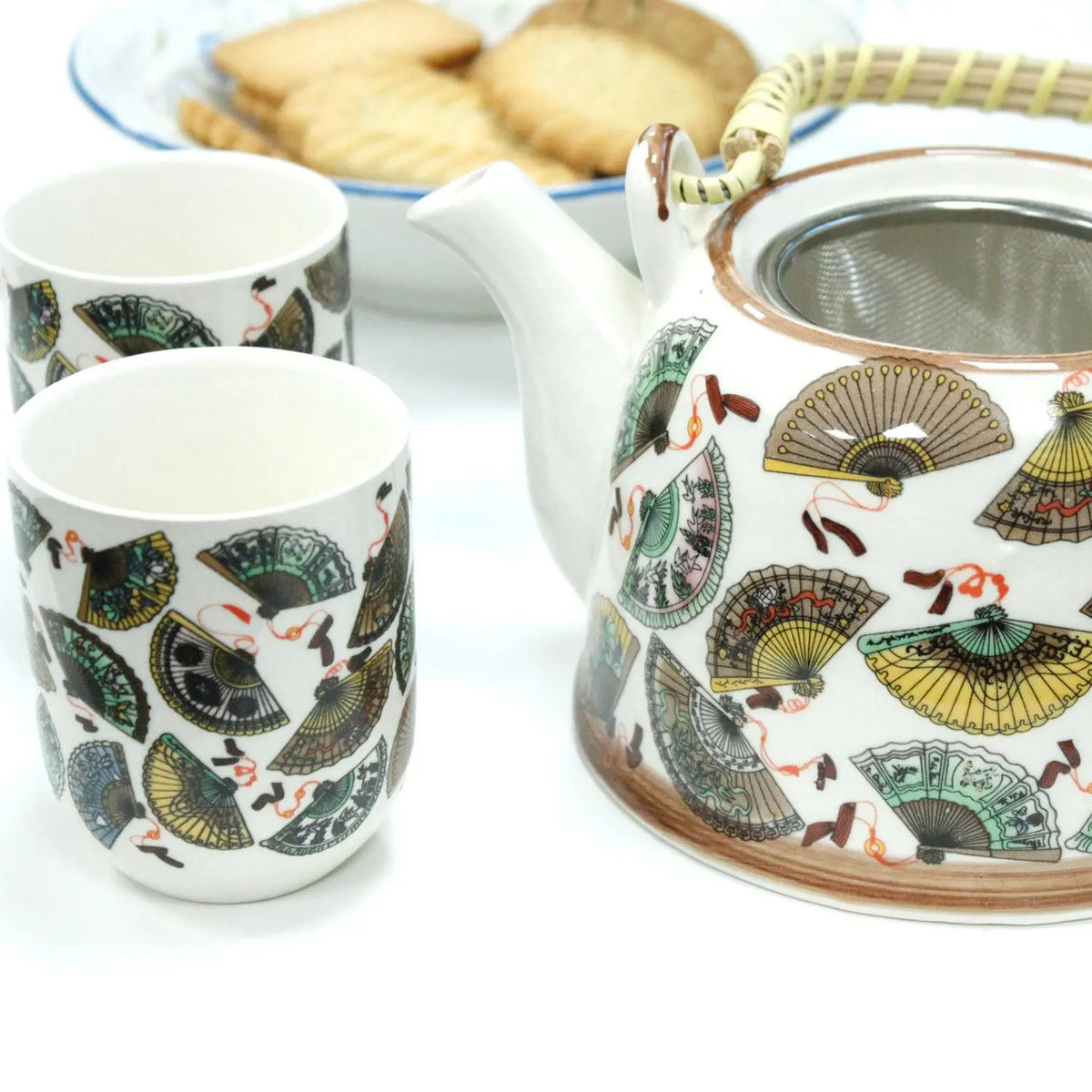 Set de tetera con colador y tazas de cerámica blanca, decoradas con abanicos chinos coloridos y asa de fibras naturales.