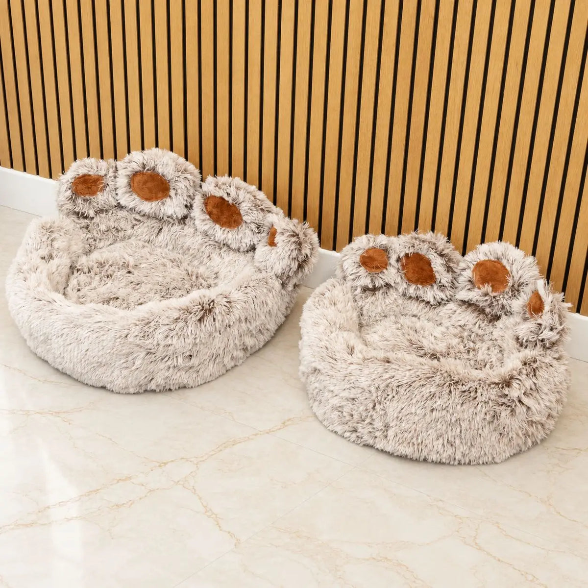 Dos camas para mascotas con forma de huella de distinto tamaño junto a una pared de listones