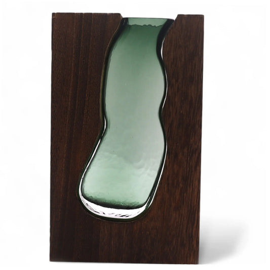 Florero de vidrio verde con forma orgánica encajado en una pieza rectangular de madera oscura con veteado visible.