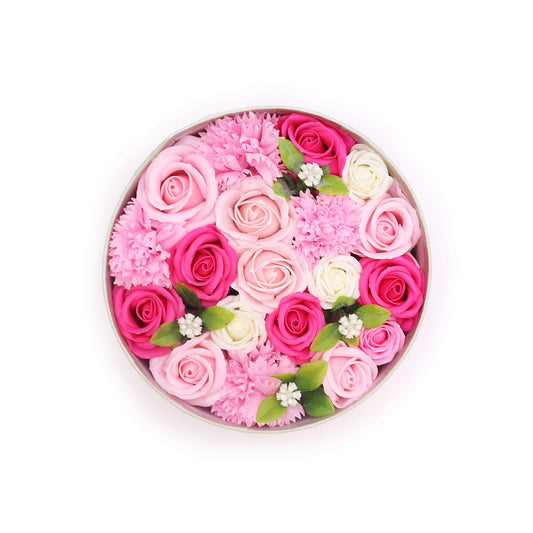 Caja redonda con rosas y flores de jabón en tonos rosa, blanco y fucsia, con hojas verdes decorativas.