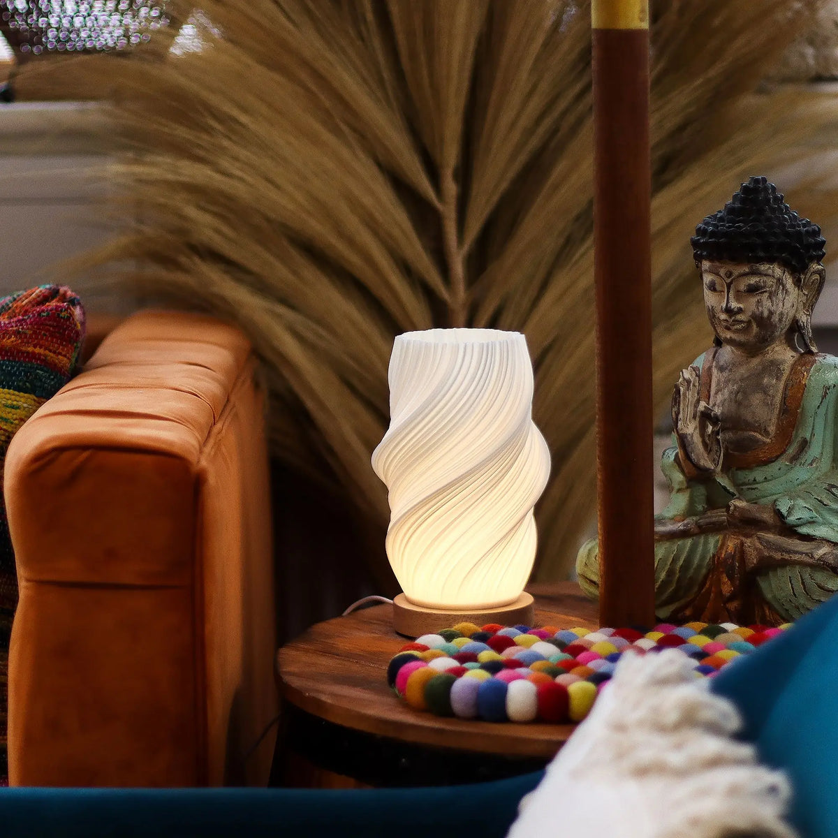 Lámpara blanca de sobremesa con forma de nube trenzada, base de madera y luz ambiental cálida en una mesa auxiliar.