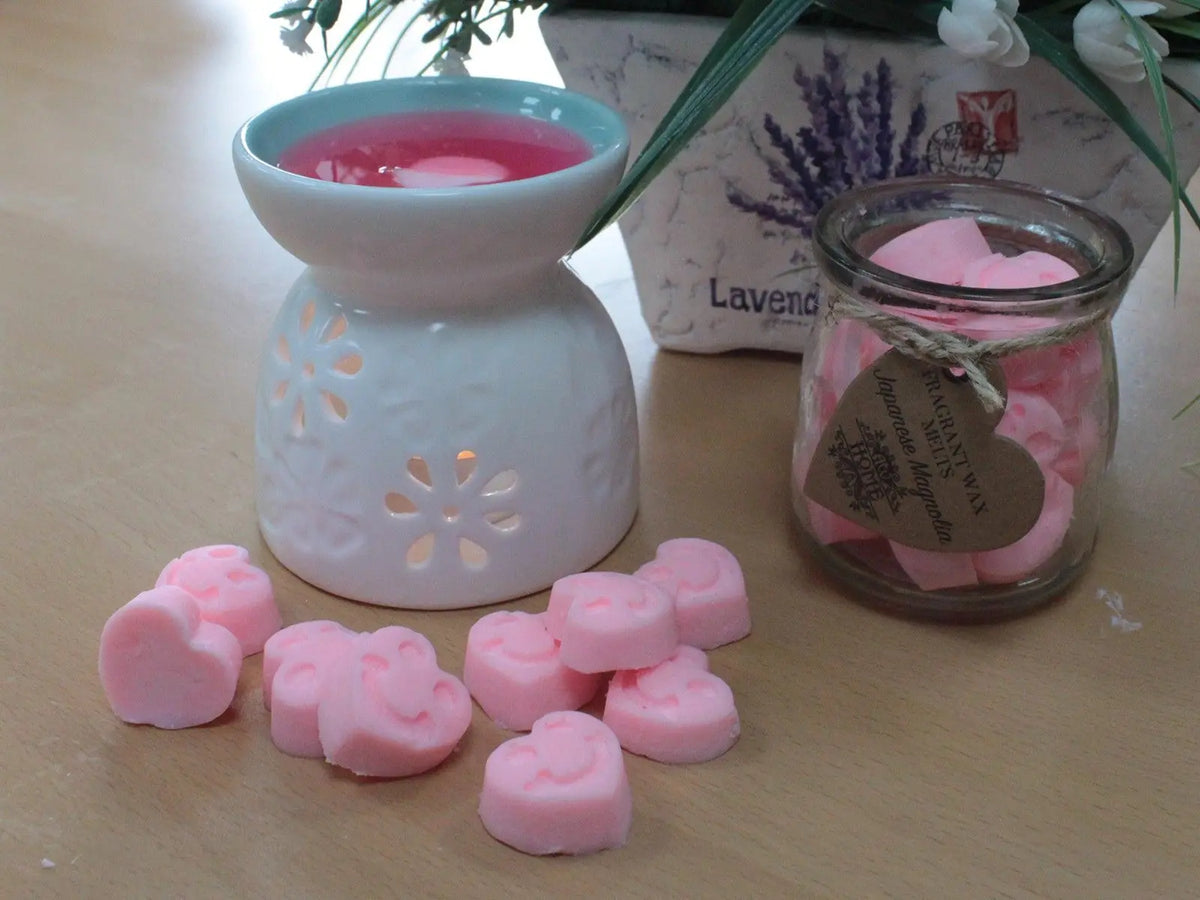Quemador de cerámica con cera rosa, frasco de vidrio con corazones de cera y detalles de flores lavanda.